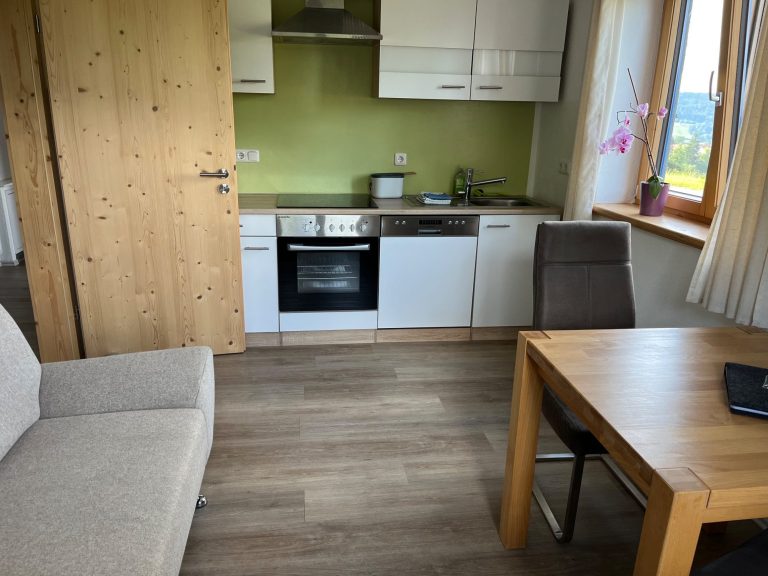 Helle Wohnküche der Ferienwohnung Neyer in Steibis mit Esstisch, Sofa und Blick ins Grüne – natürlich wohnen im Allgäu